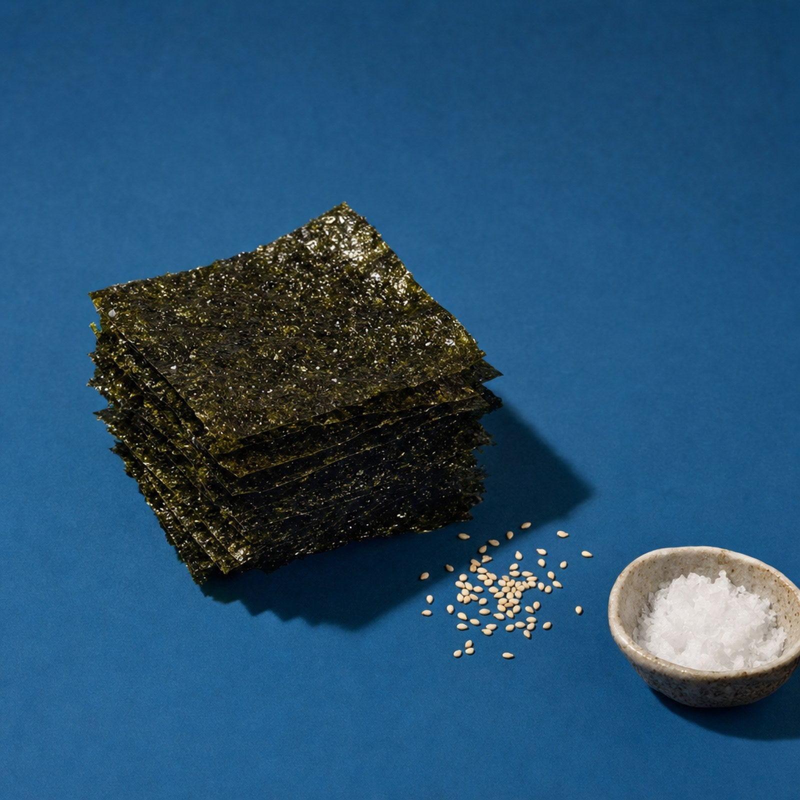 Stack of roasted seaweed snack squares with sesame seeds on a deep ocean-blue editorial backdrop